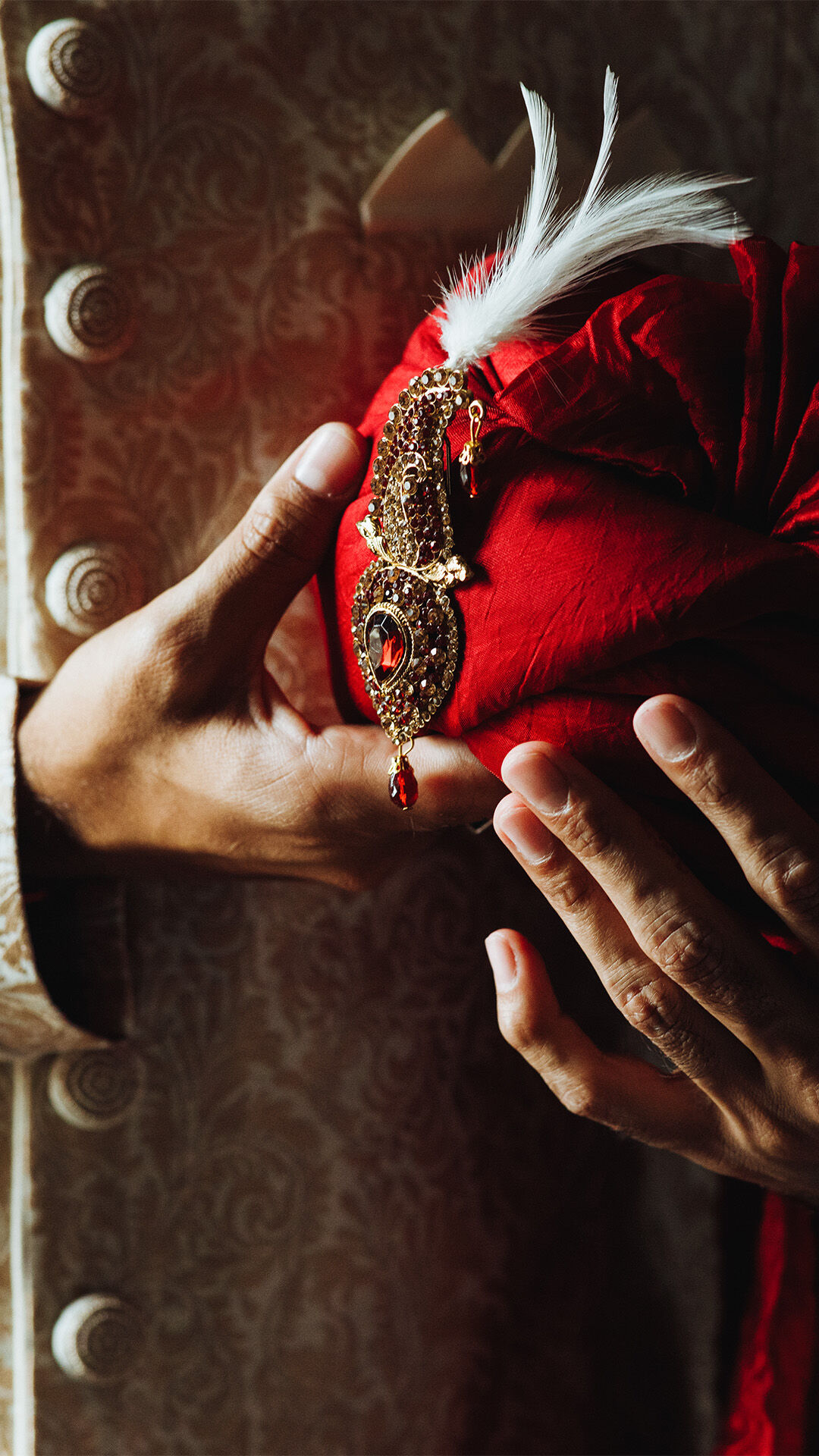 Man holding a red safa with striking red diamond and white feather detail.
